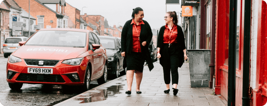 Two gisl in red walking next to a red belvoir car